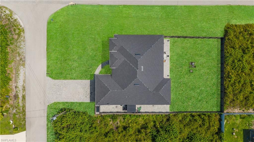 Overhead perspective showcasing the property's dark shingle roof, expansive green lawn, stone paver patio, and paved driveway