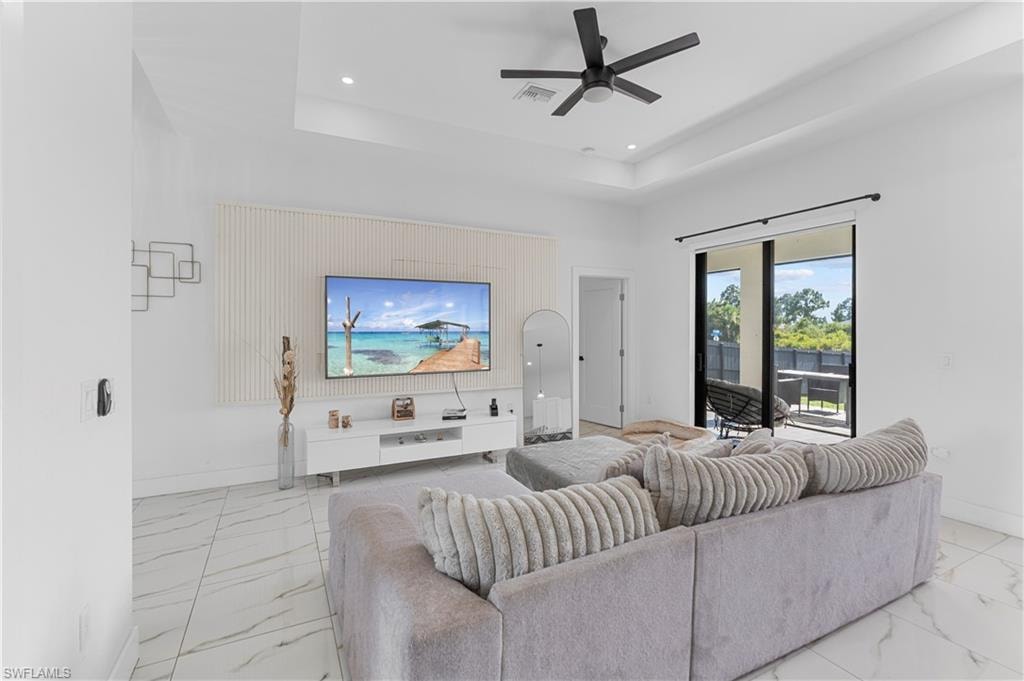 Spacious living area featuring large format white tile flooring, a tray ceiling with a ceiling fan, and a built-in entertainment wall