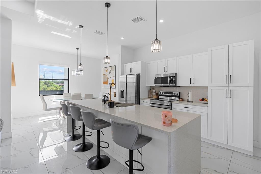 Modern kitchen featuring a large island with seating, white shaker-style cabinetry, stainless steel appliances, and a tile backsplash
