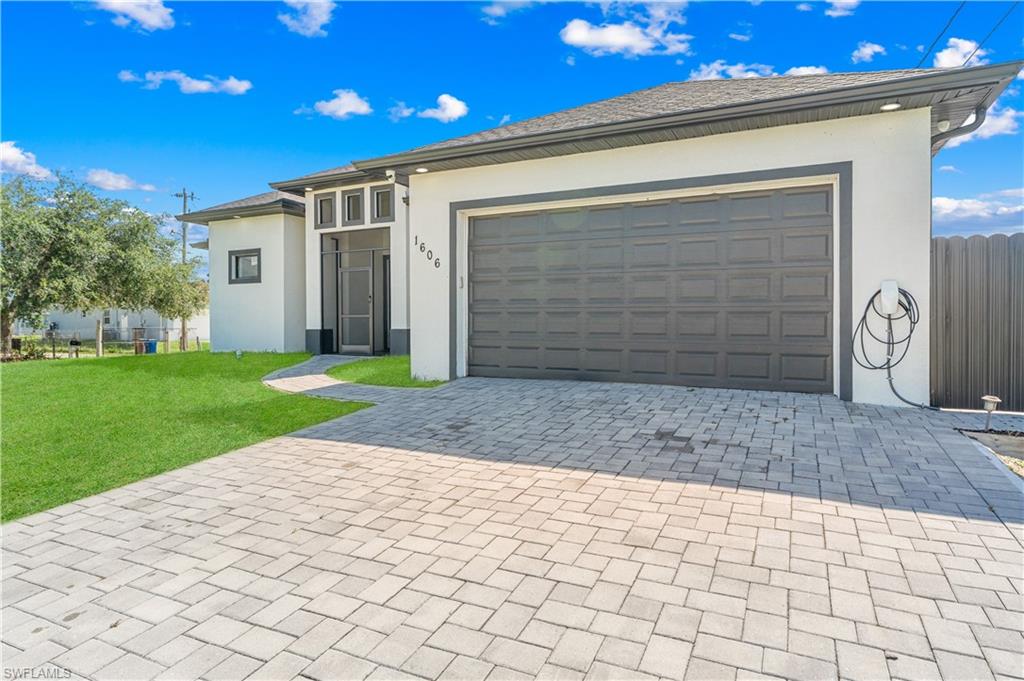Contemporary exterior featuring a paver driveway, an attached garage, a covered entry with transom windows, and a manicured lawn