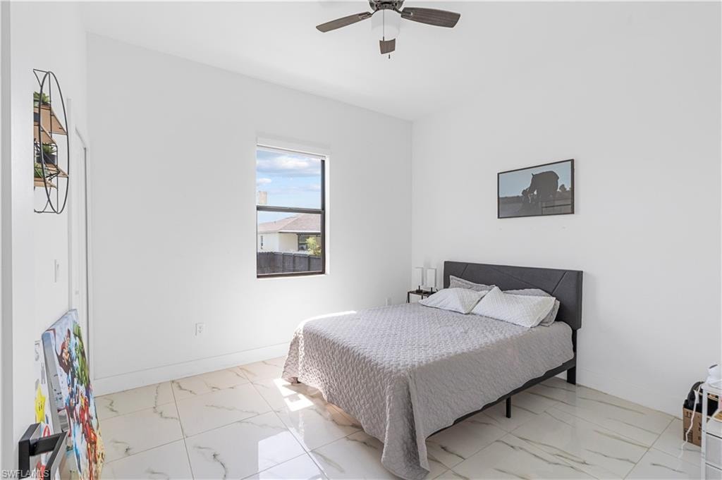 Room featuring a square window, a ceiling fan with dark wood-finish blades, and large format tile flooring