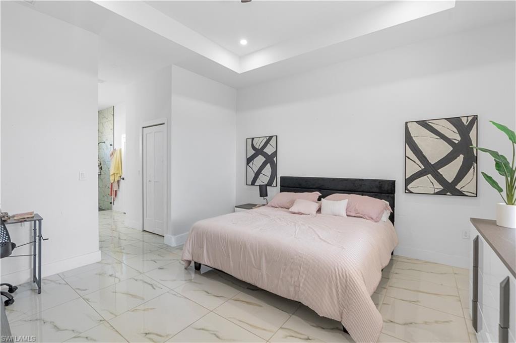 Spacious room featuring large format tile flooring, a tray ceiling, recessed lighting, white walls, and a bi-fold closet door