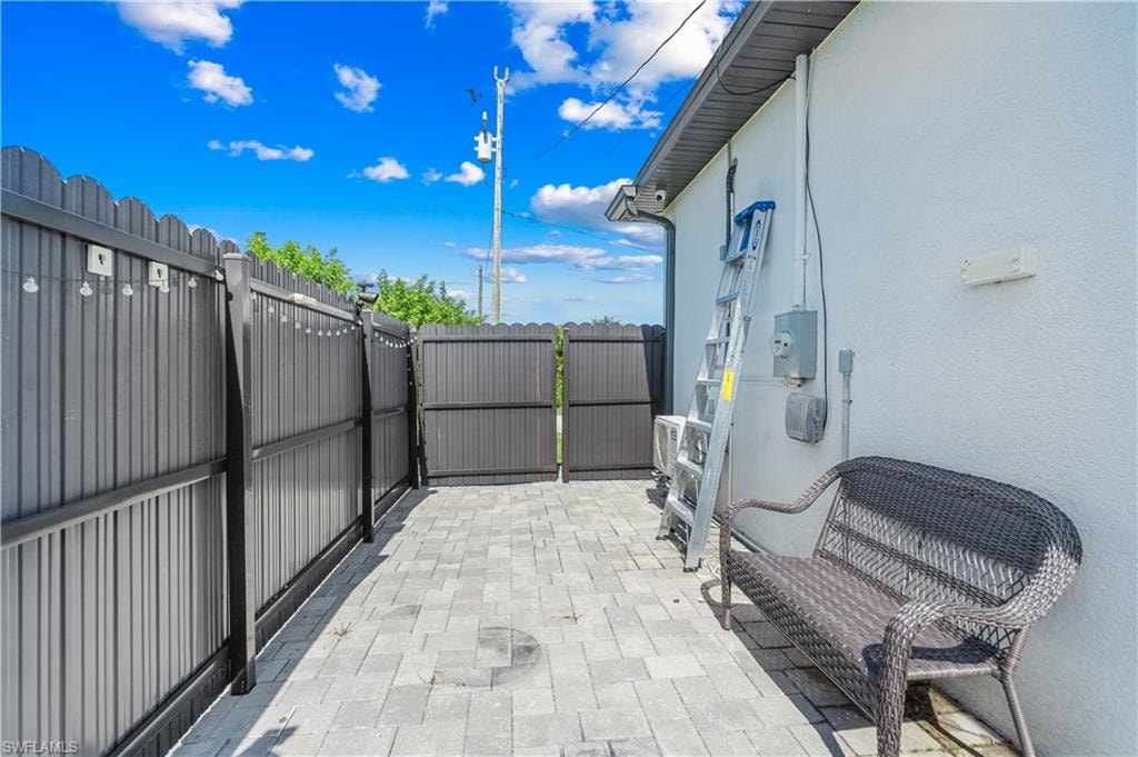 Paved outdoor area featuring a full-height privacy fence with a double-gate entry, textured stucco exterior, and an air conditioning unit