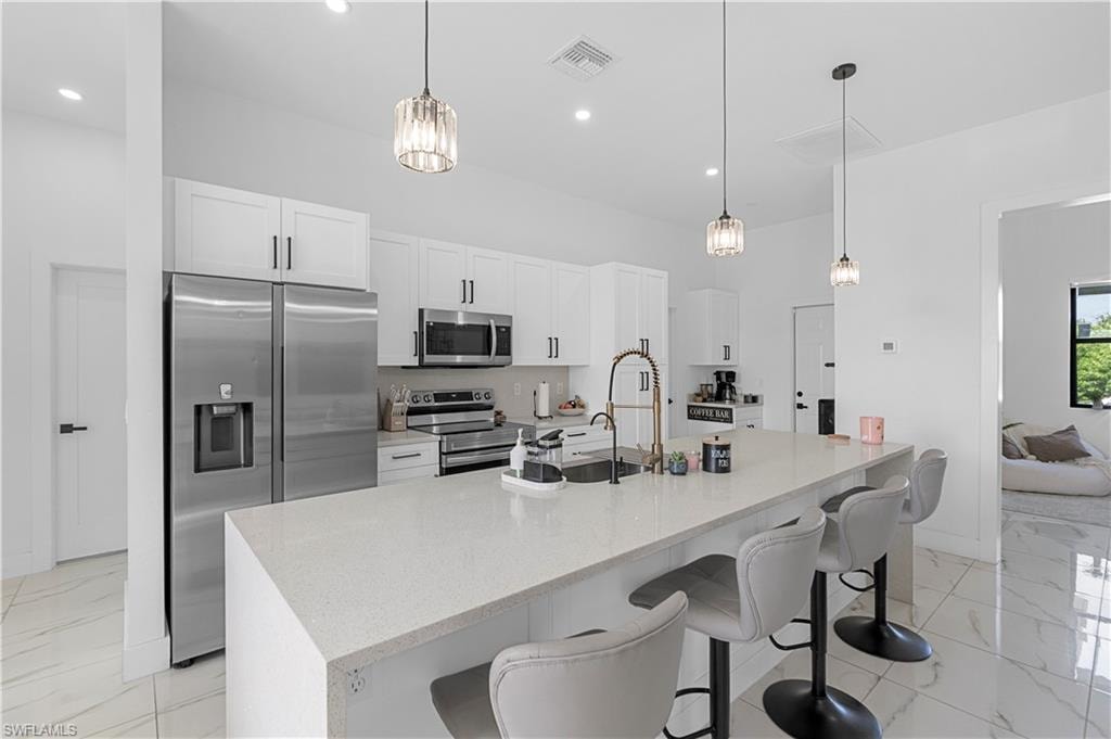 Modern kitchen featuring white cabinetry, stainless steel appliances, a large island with a surface suitable for seating, pendant lighting, and polished tile flooring