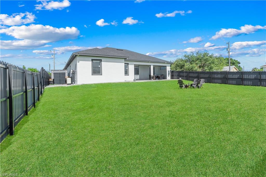 Expansive backyard featuring a lush green lawn, full perimeter fencing, and a covered patio area