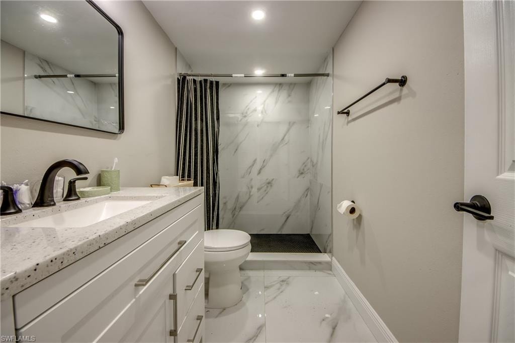 Bathroom featuring a single vanity with stone-finish countertop, white cabinetry, and matte black fixtures