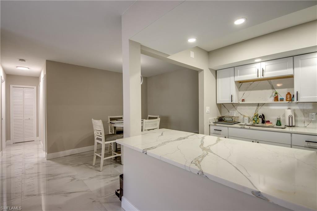 Kitchen island featuring a veined countertop, white cabinetry with dark hardware, and a matching full-height backsplash