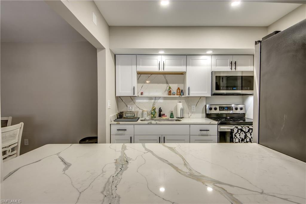 Contemporary kitchen featuring a large island with a patterned countertop, white cabinetry with dark hardware, stainless steel appliances, and recessed lighting