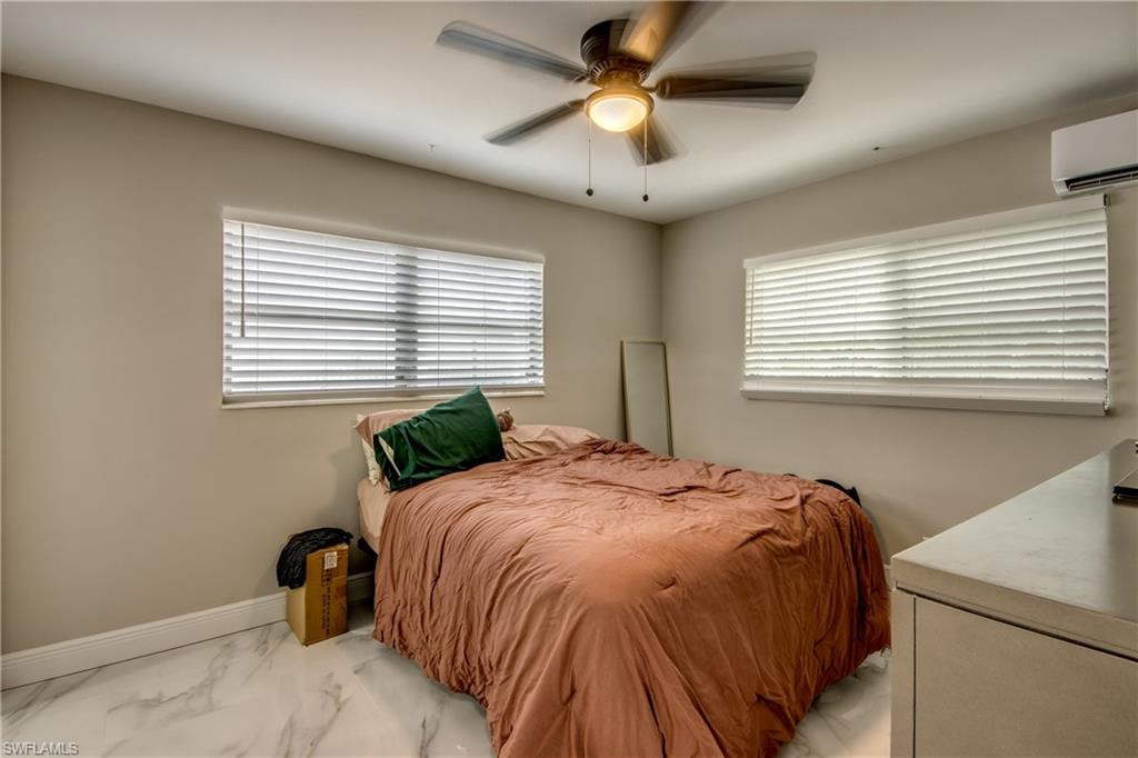 Room featuring two windows with white blinds, a ceiling fan with integrated lighting, a wall-mounted air conditioning unit, and polished tile flooring with a white and grey veining pattern