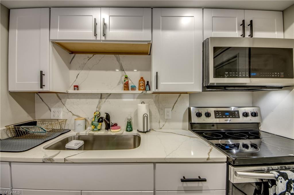 Kitchen featuring white shaker-style cabinetry, a stainless steel sink, a stainless steel microwave, and an electric range