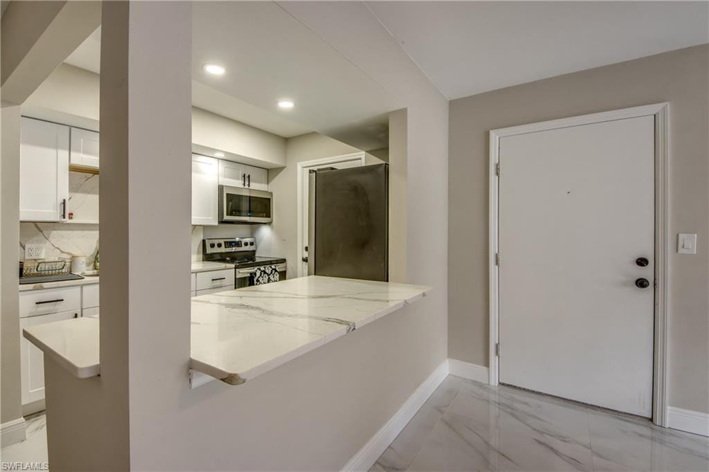 Kitchen passthrough with a marble-finish countertop, white cabinetry, integrated stainless steel appliances, and recessed lighting