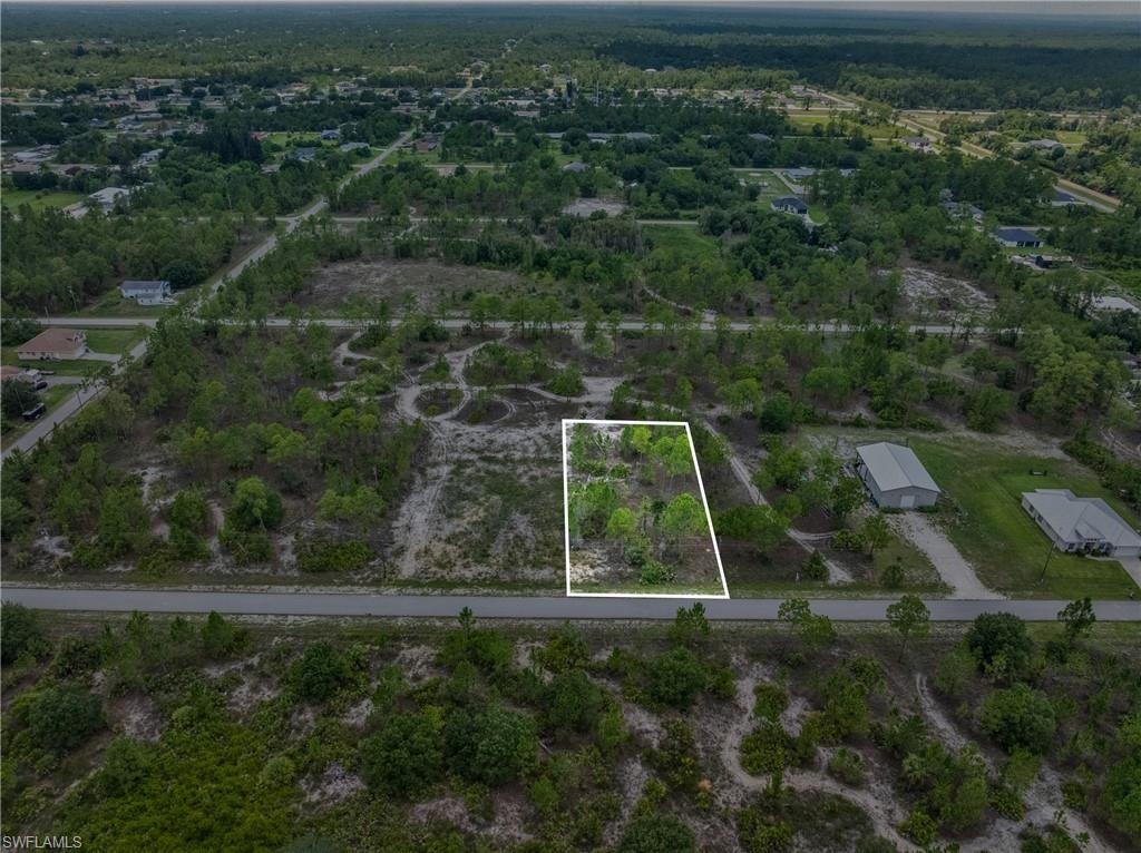 Vacant land parcel featuring mature trees, a clear road frontage, and surrounding undeveloped acreage