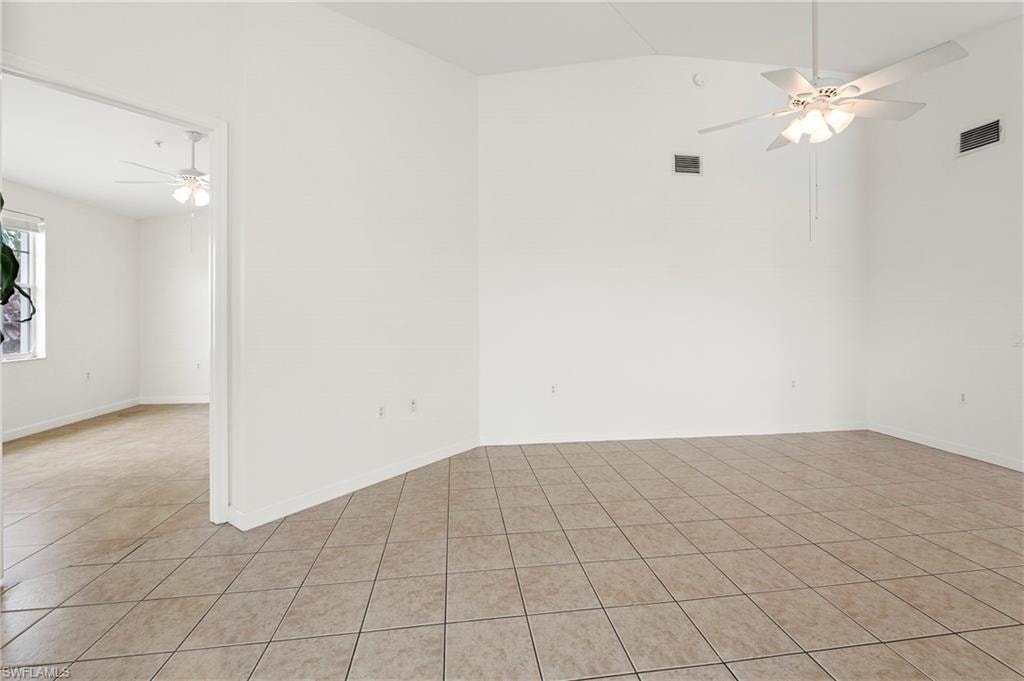 Spacious interior room featuring light-toned tile flooring, vaulted ceilings, and a ceiling fan with integrated lighting