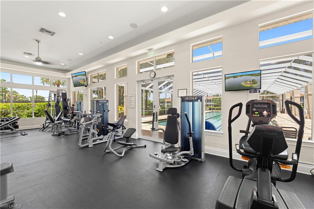 Fitness center featuring various exercise equipment, resilient rubber flooring, multiple windows providing exterior light, and wall-mounted televisions