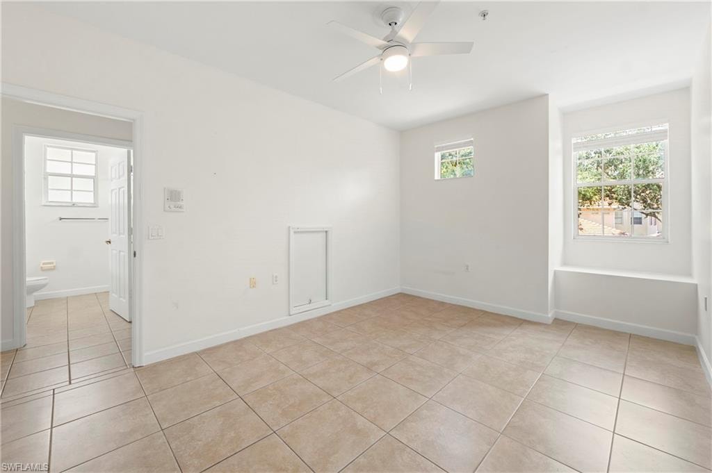 Open concept room featuring neutral tone tile flooring, a ceiling fan with integrated lighting, multiple windows providing natural light, and a built-in window seat