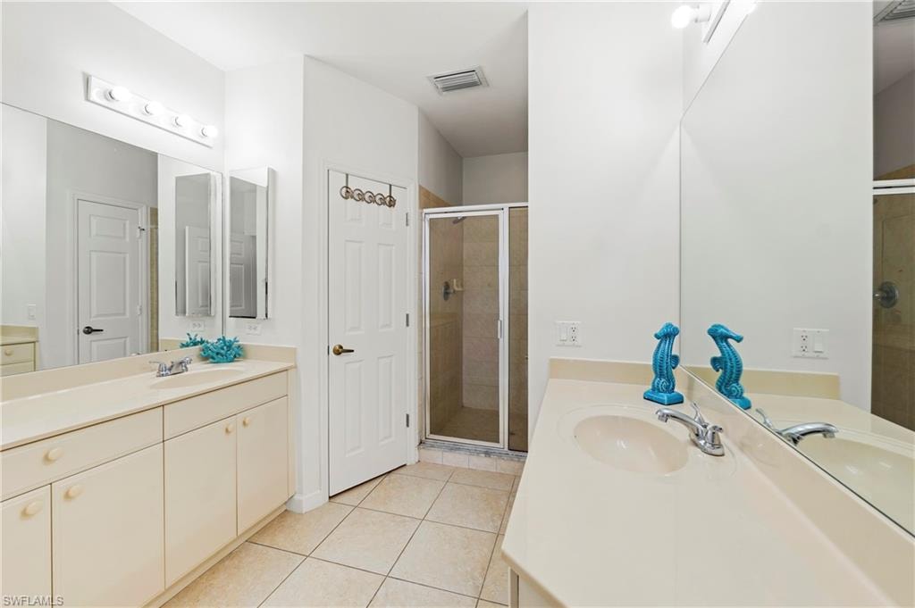 Bathroom featuring dual vanity sinks set into a light-toned countertop, a glass-enclosed shower, a built-in wall mirror, and neutral tile flooring