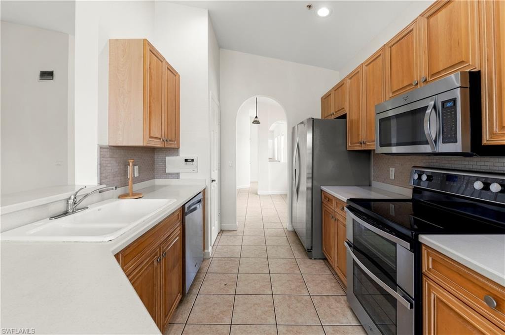 Functional kitchen featuring stainless steel appliances, tile flooring, light wood cabinetry, white countertops, and a tiled backsplash