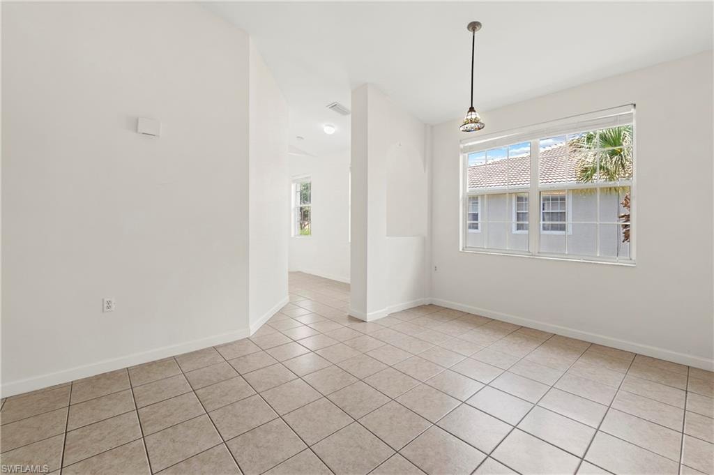 Spacious room featuring neutral-toned tile flooring, a large window with white blinds, and a decorative pendant light fixture