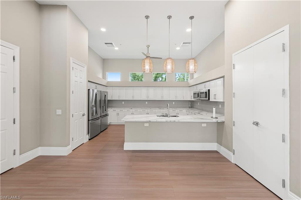 Open-concept kitchen featuring wood-finish flooring, white cabinetry, light countertops, stainless steel appliances, and a vaulted ceiling with pendant lighting