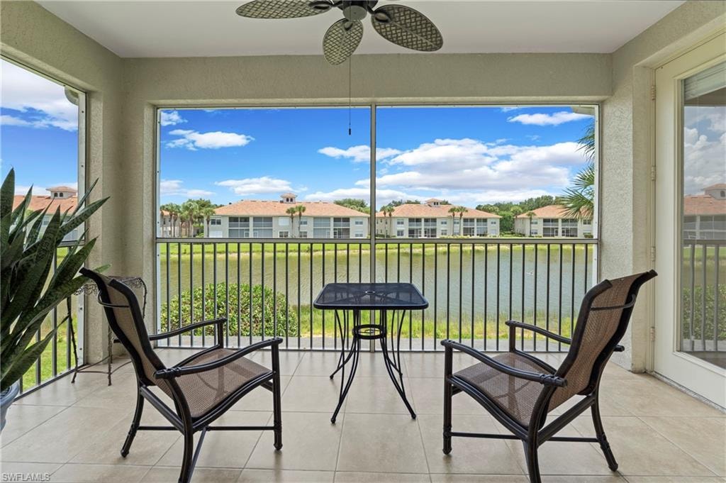 Screened balcony featuring tile flooring and a ceiling fan, overlooking a body of water with architectural structures beyond
