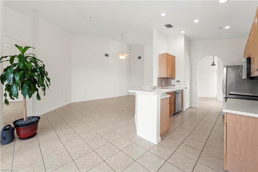 Kitchen and living area featuring tile flooring, light wood-finish cabinetry, stainless steel appliances, and an arched entryway