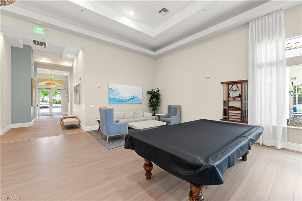 Spacious common area featuring a billiards table, tray ceiling details, wood-finish flooring, high ceilings, and tall windows with sheer drapery