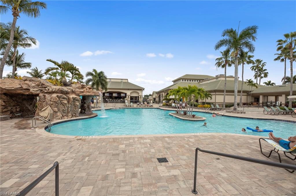 Resort-style swimming pool featuring a rock grotto with waterfall, lush palm trees, and an expansive paver deck