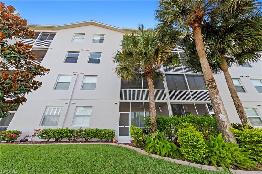 Multi-story residential building featuring a light-colored exterior finish, multiple screened balconies, and a manicured lawn with mature palm trees and diverse landscaping