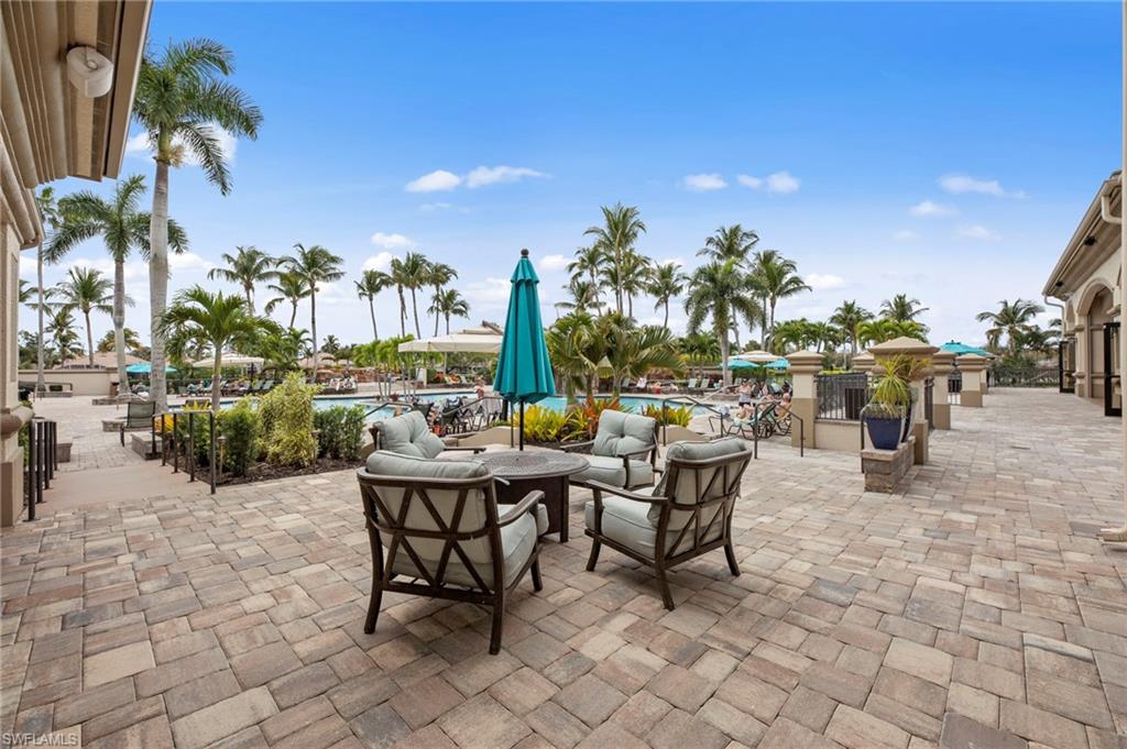 Expansive paver patio featuring an outdoor seating area with a table and chairs, surrounded by lush landscaping and palm trees