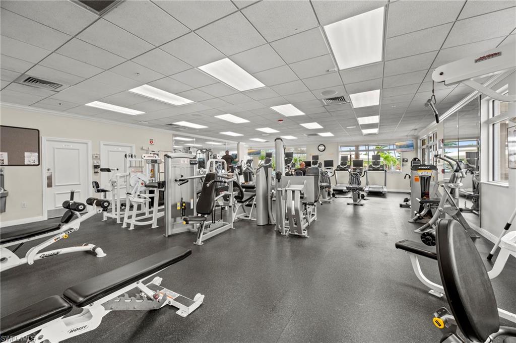 Spacious fitness center featuring various exercise equipment, resilient rubber flooring, drop ceiling with integrated lighting, mirrored wall panels, and large windows along one wall