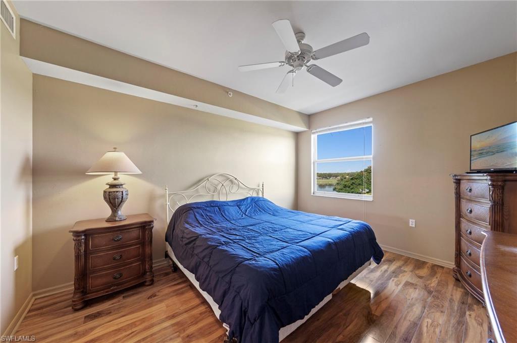 Bedroom featuring wood-finish flooring, a ceiling fan, and a window overlooking a water feature and distant trees