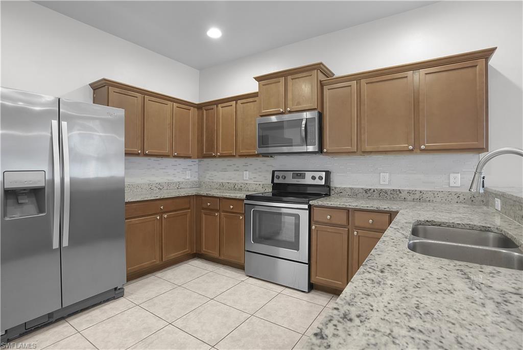 Kitchen featuring stainless steel appliances, light wood-finish cabinetry, speckled countertops, a tile backsplash, and tile flooring
