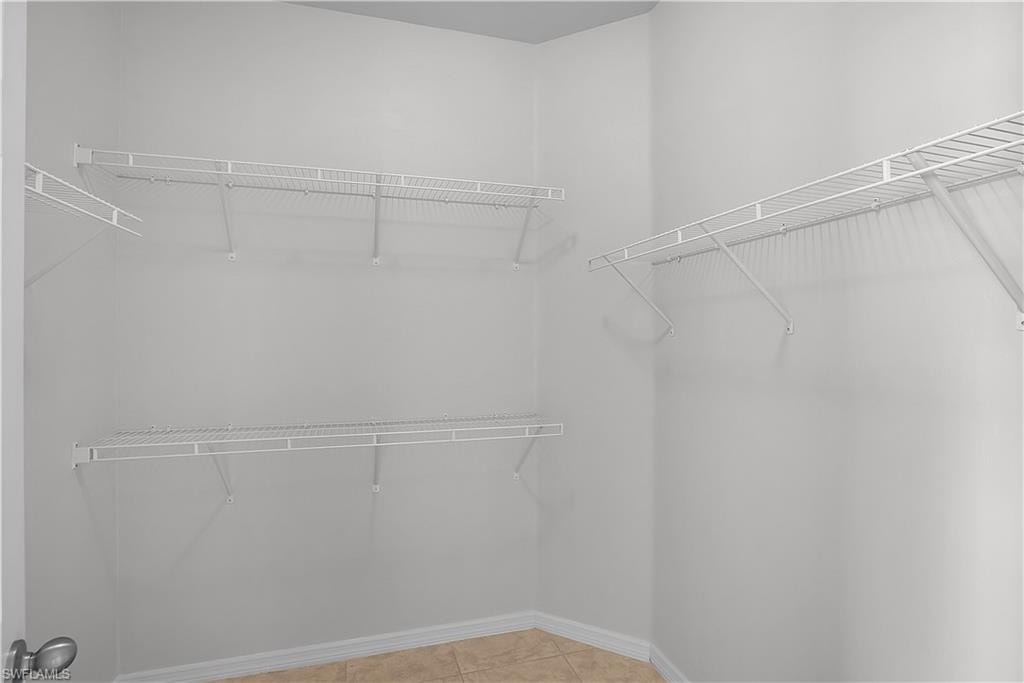 Spacious walk-in closet featuring light gray walls, white wire shelving, and a tiled floor