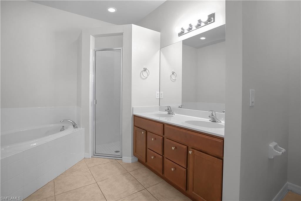 Bathroom featuring a double vanity with wood cabinetry and white countertops, a large mirror, a separate shower with a glass enclosure, a built-in bathtub, and tile flooring
