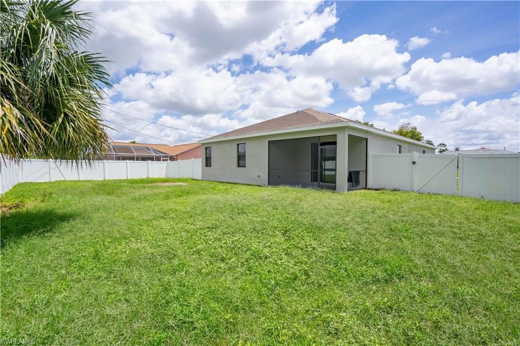 Expansive grassy backyard featuring a full privacy fence, screened patio, and a palm tree