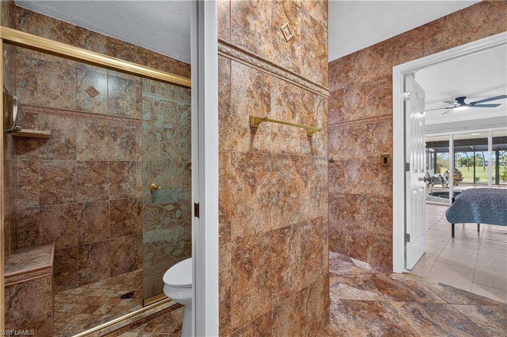 Tiled bathroom featuring a glass-enclosed shower with gold-tone accents and an integrated bench