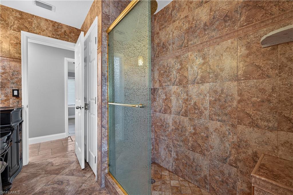 Shower enclosure featuring a framed glass door with golden-finish hardware, textured glass, and a tiled interior with an integrated bench