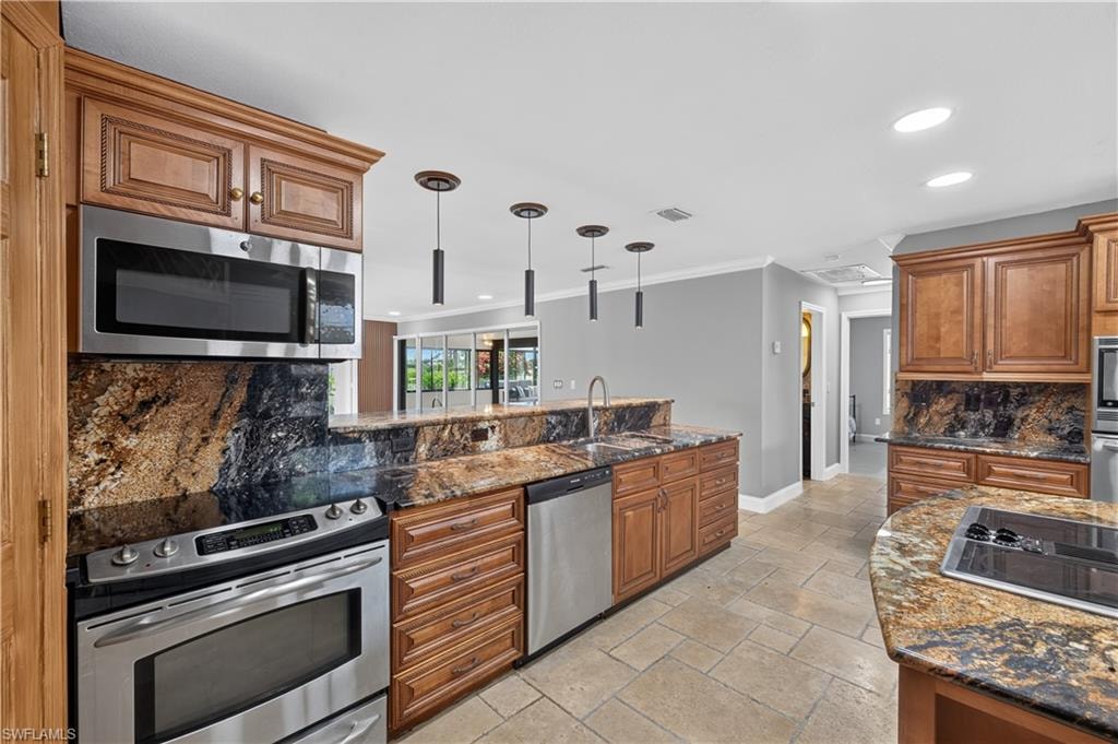 Kitchen featuring wood cabinetry, stainless steel appliances, dark stone countertops with matching backsplash, and recessed lighting