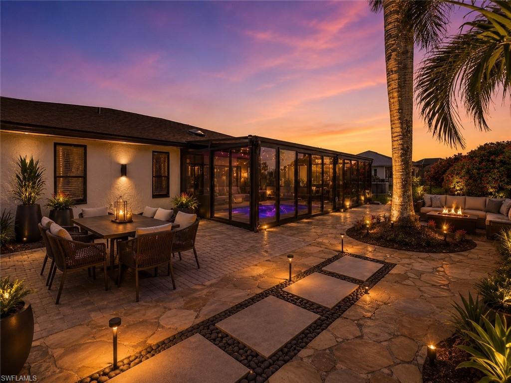 Expansive outdoor living area featuring a large patio with flagstone and paver sections, a screened enclosure housing a pool, a built-in outdoor seating area, mature palm trees, and integrated landscape lighting, Virtually staged.