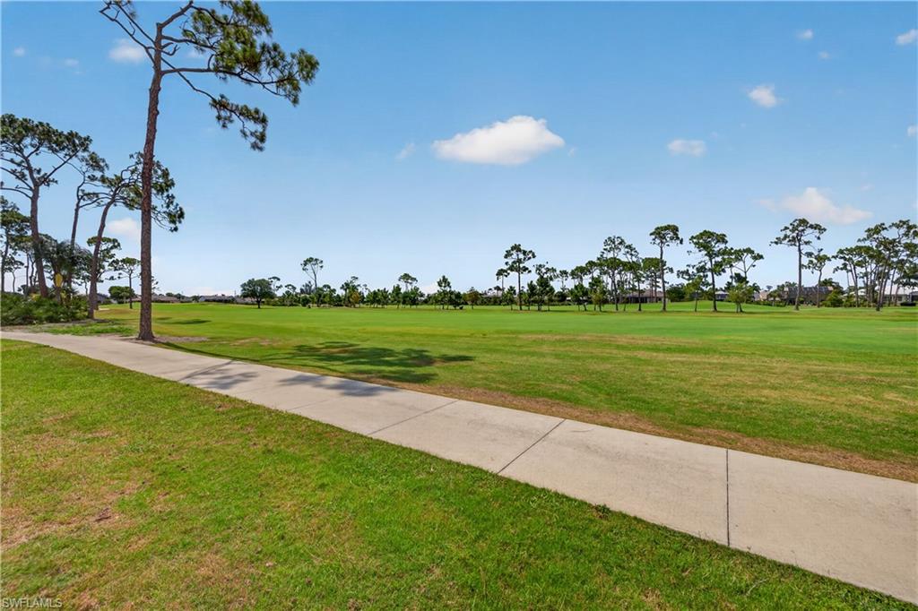 Expansive green golf course featuring a concrete path and mature pine trees