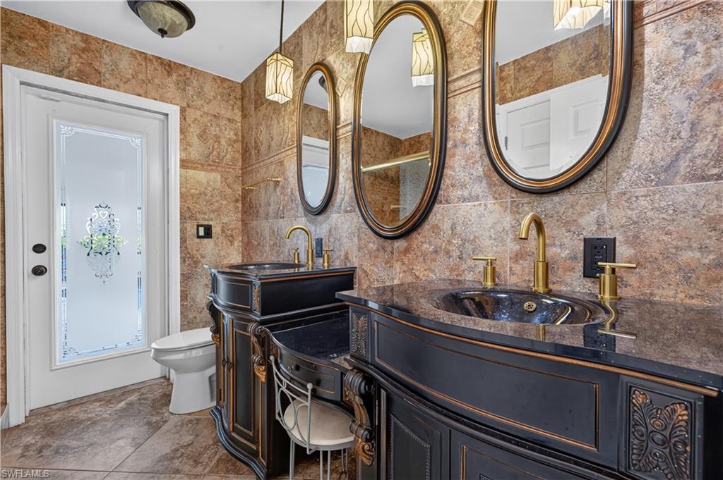 Custom vanity with dual vessel sinks, ornate black cabinetry, and gold-finish fixtures