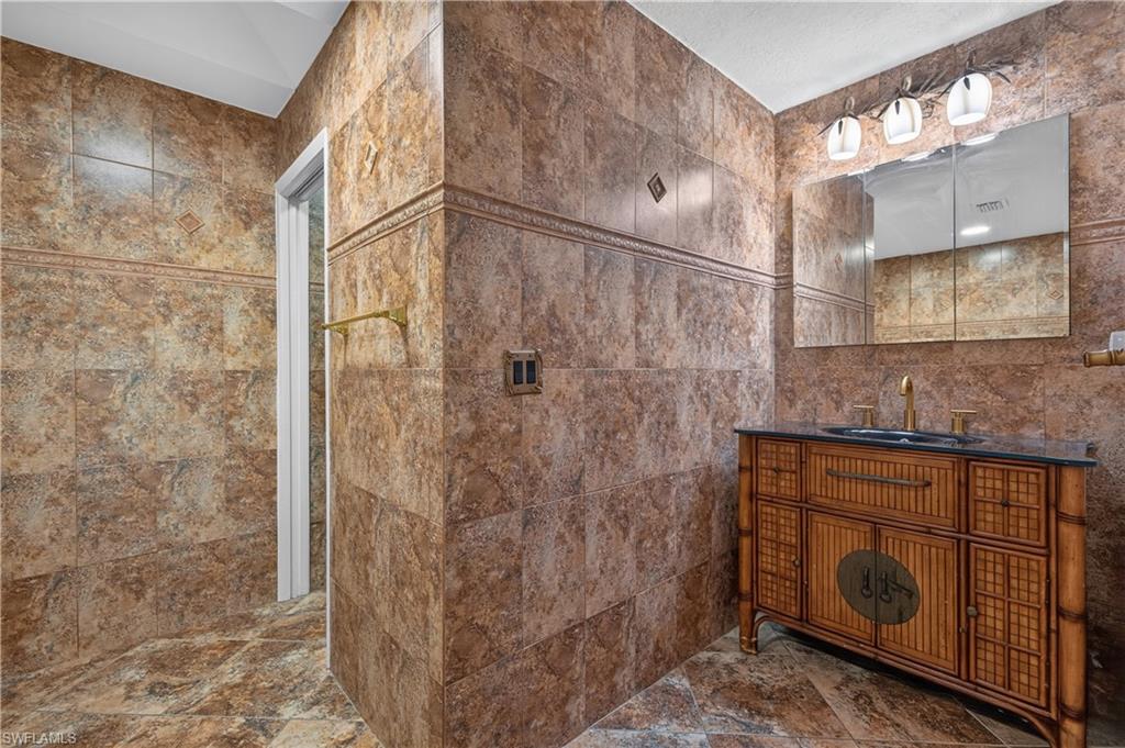Bathroom vanity with a dark countertop and gold-toned faucet, complemented by a triple-door mirrored medicine cabinet and three-light vanity fixture