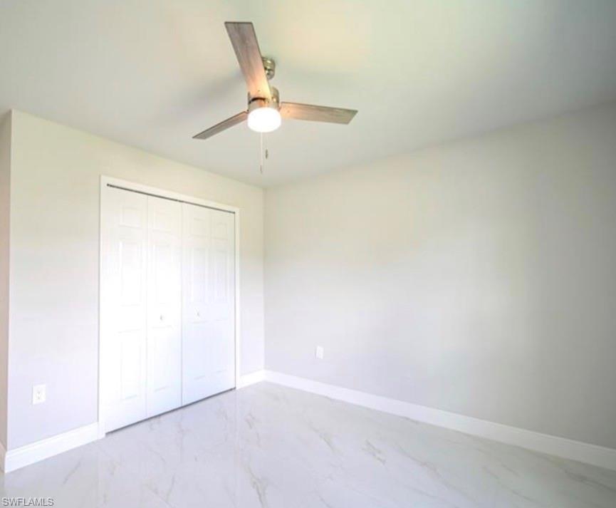 Interior space featuring light gray walls, a ceiling fan with light fixture, white bi-fold closet doors, white baseboards, and light-toned tile flooring