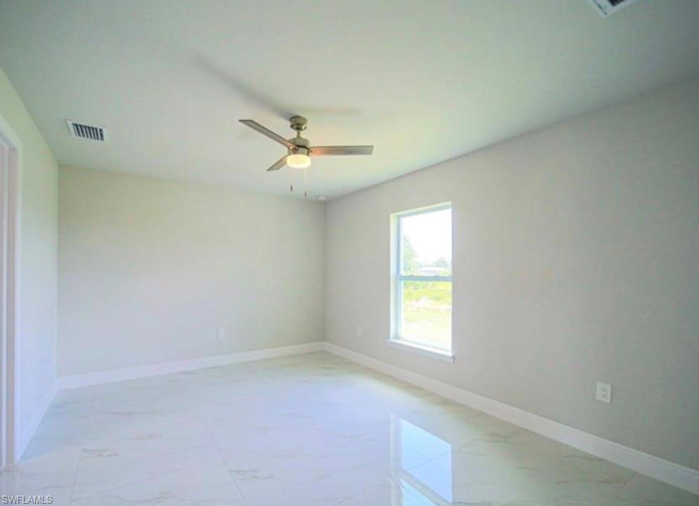 Bright interior space featuring large format tile flooring, a ceiling fan with integrated lighting, a single window, and a crisp white baseboard trim