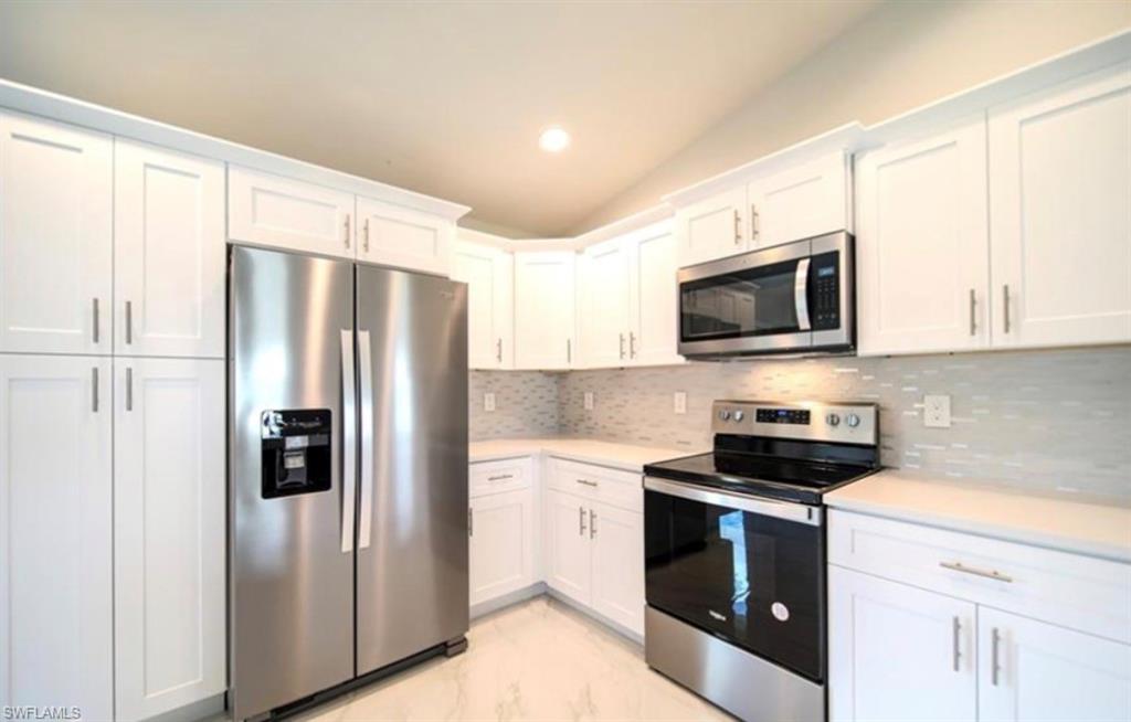 Modern kitchen featuring white shaker cabinetry with brushed nickel hardware, stainless steel appliances, light-toned countertops, a full-height tile backsplash, and recessed lighting