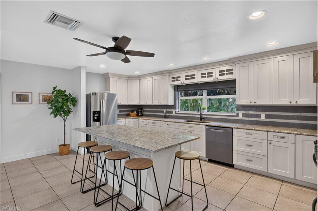 Spacious kitchen featuring an expansive island with seating, light cabinetry, granite countertops, tile flooring, and recessed lighting