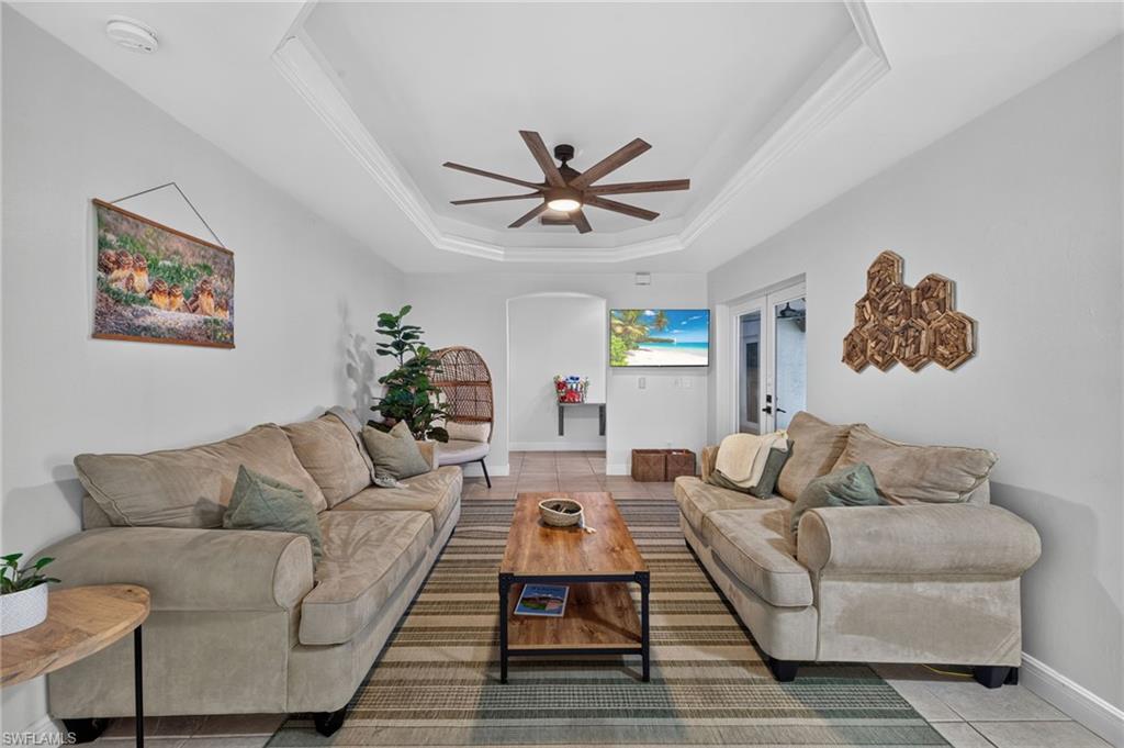 Living area featuring a tray ceiling with crown molding, a ceiling fan, and tile flooring