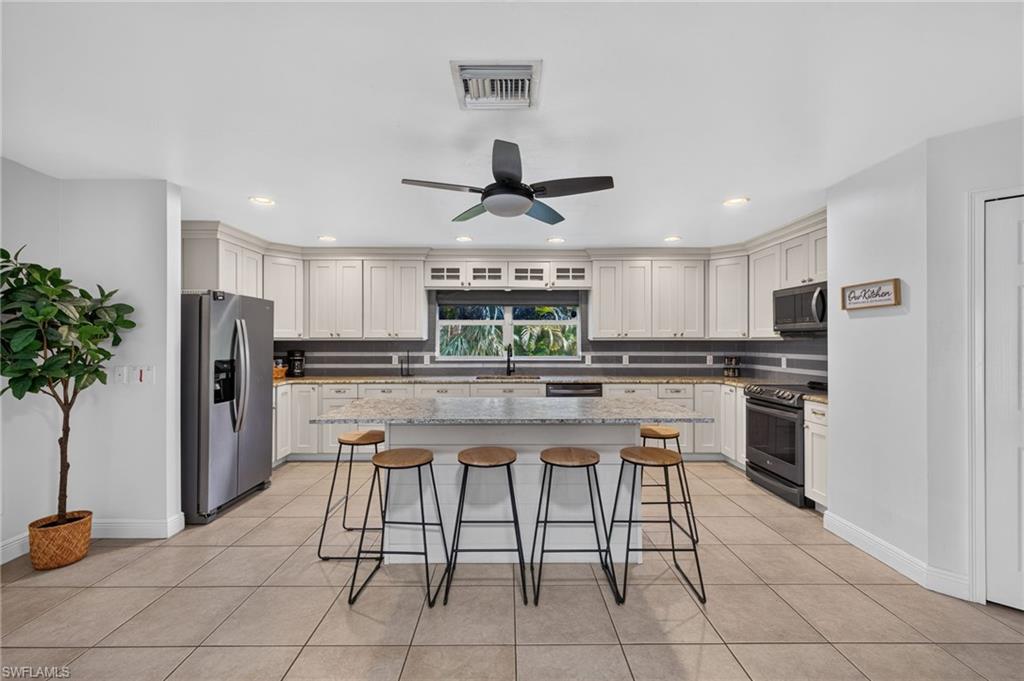 Spacious kitchen featuring an extended island with stone countertop, white shaker-style cabinetry, stainless steel refrigerator, and recessed lighting