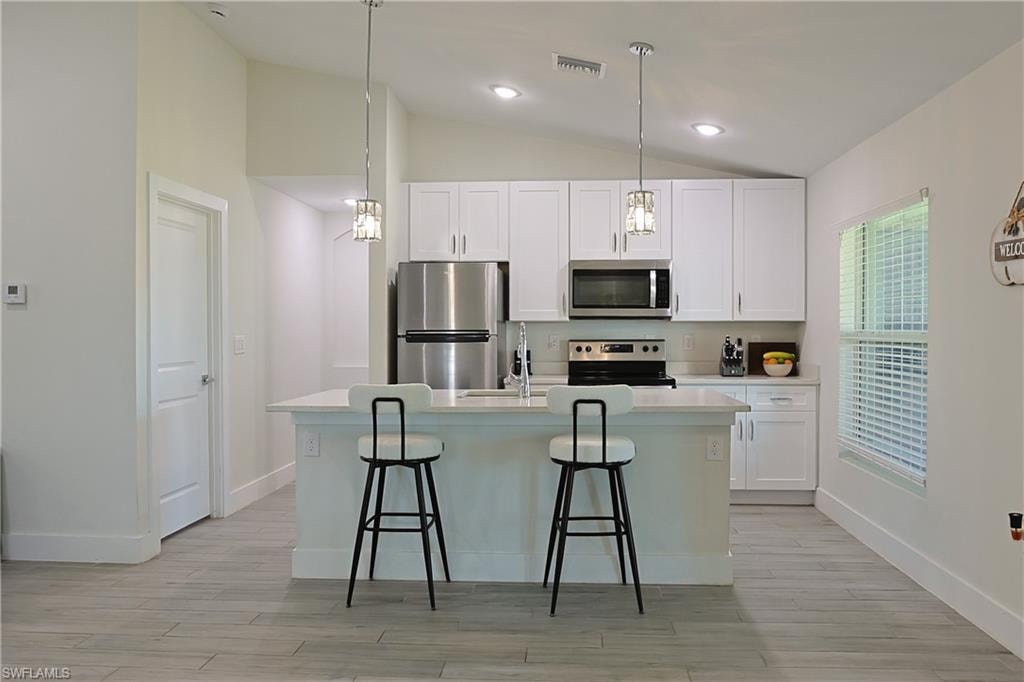 Kitchen featuring white shaker-style cabinetry, stainless steel appliances, a white island with pendant lighting, and wood-finish flooring