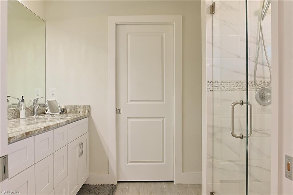 Modern bathroom featuring a glass-enclosed shower with tile surround and decorative mosaic band, a white two-panel door, and a vanity with a light-toned stone countertop, square undermount sink, and brushed nickel faucet